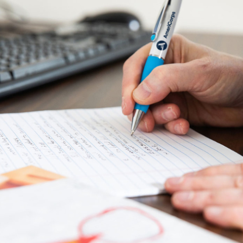 Person writing on paper with an AmeriCorps-branded pen